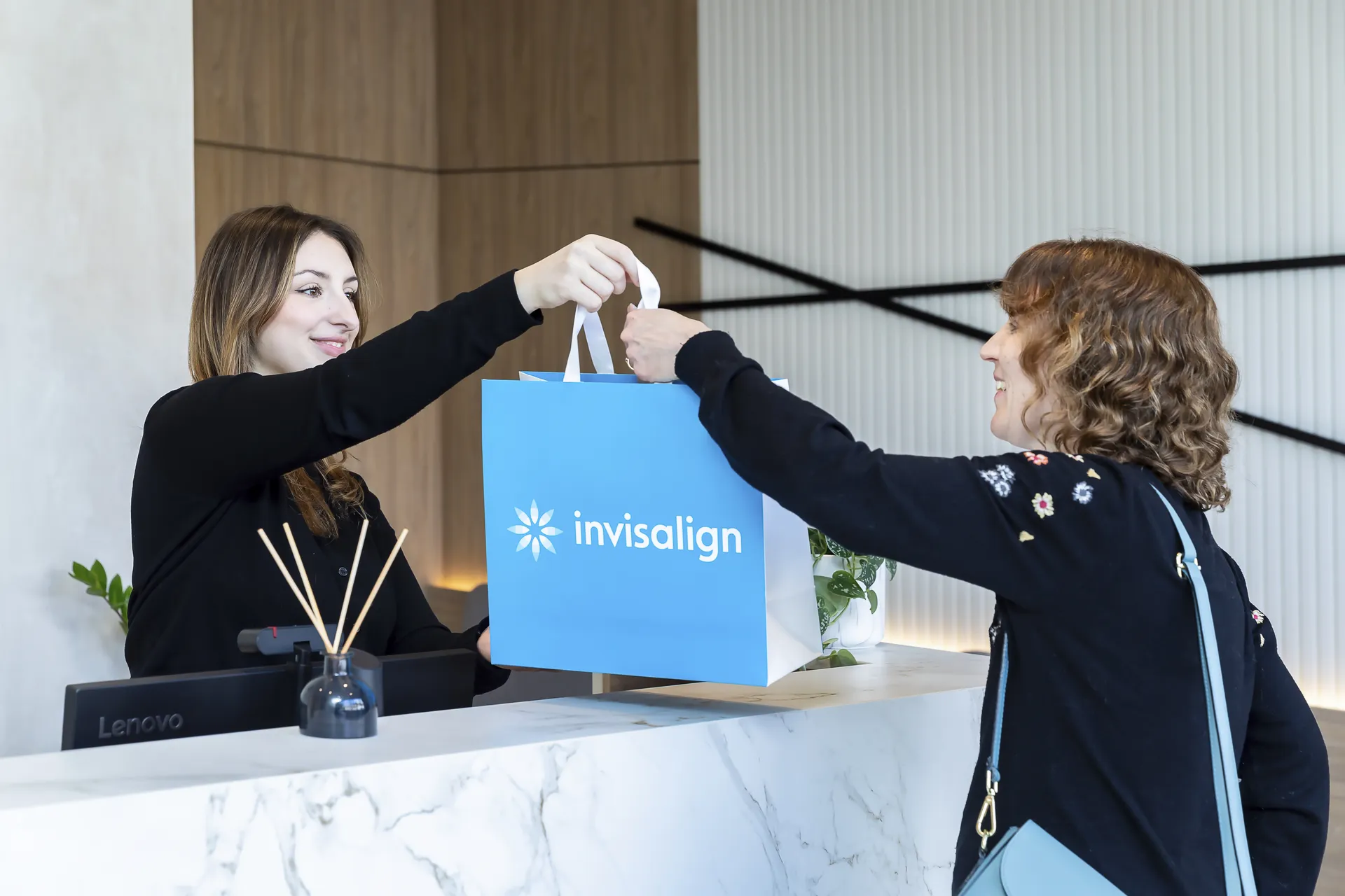Receptionist handing a patient an Invisalign bag at Bella Dental