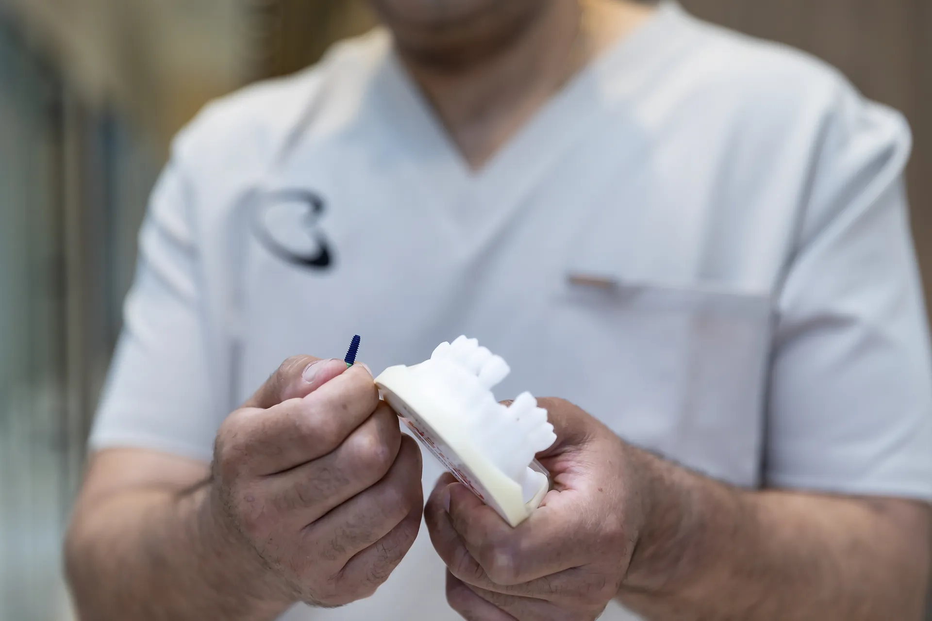 Clinician holding a dental implant beside a model of teeth