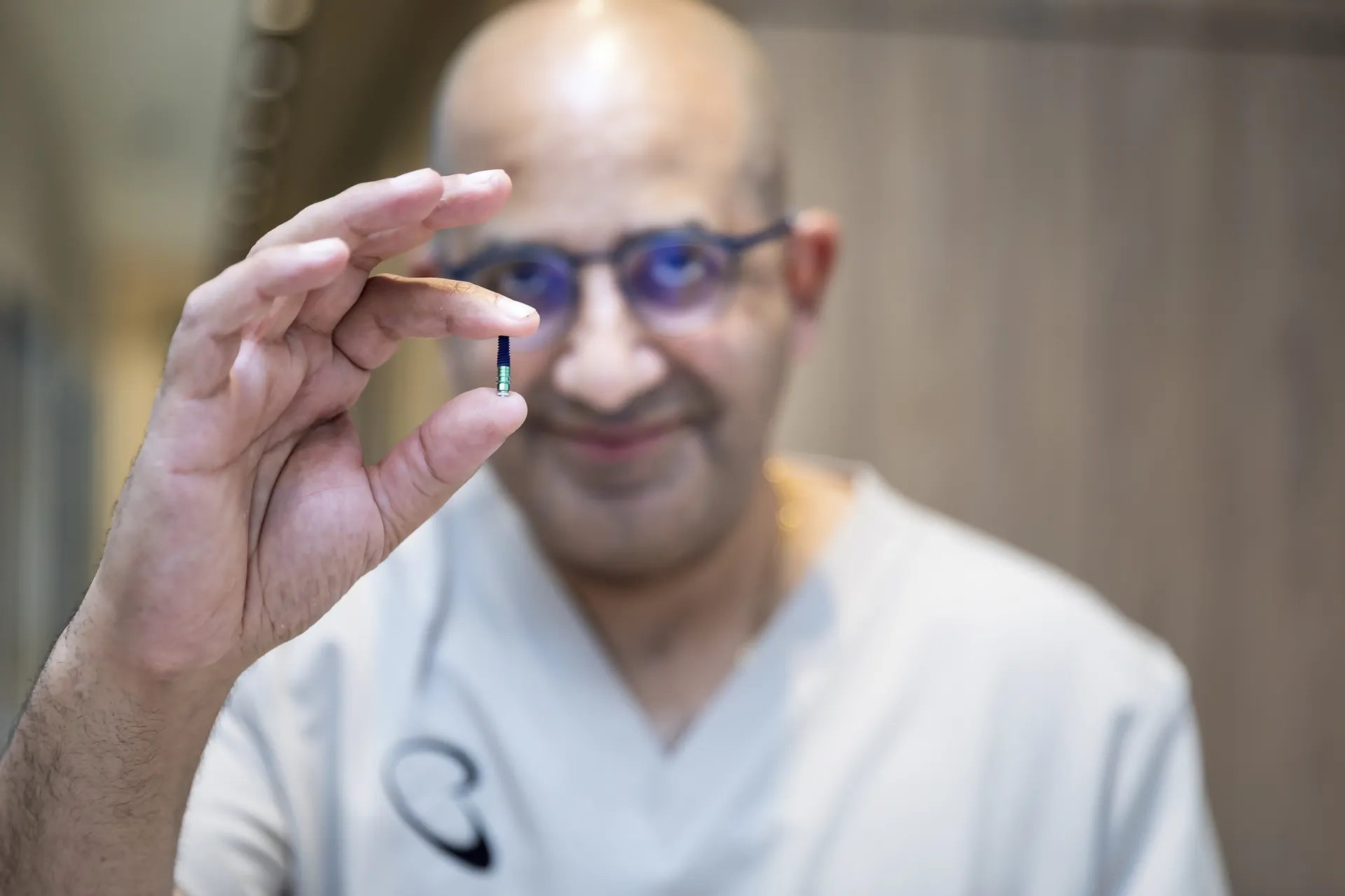 Dr Michael Boulis holding a small dental implant between his fingers